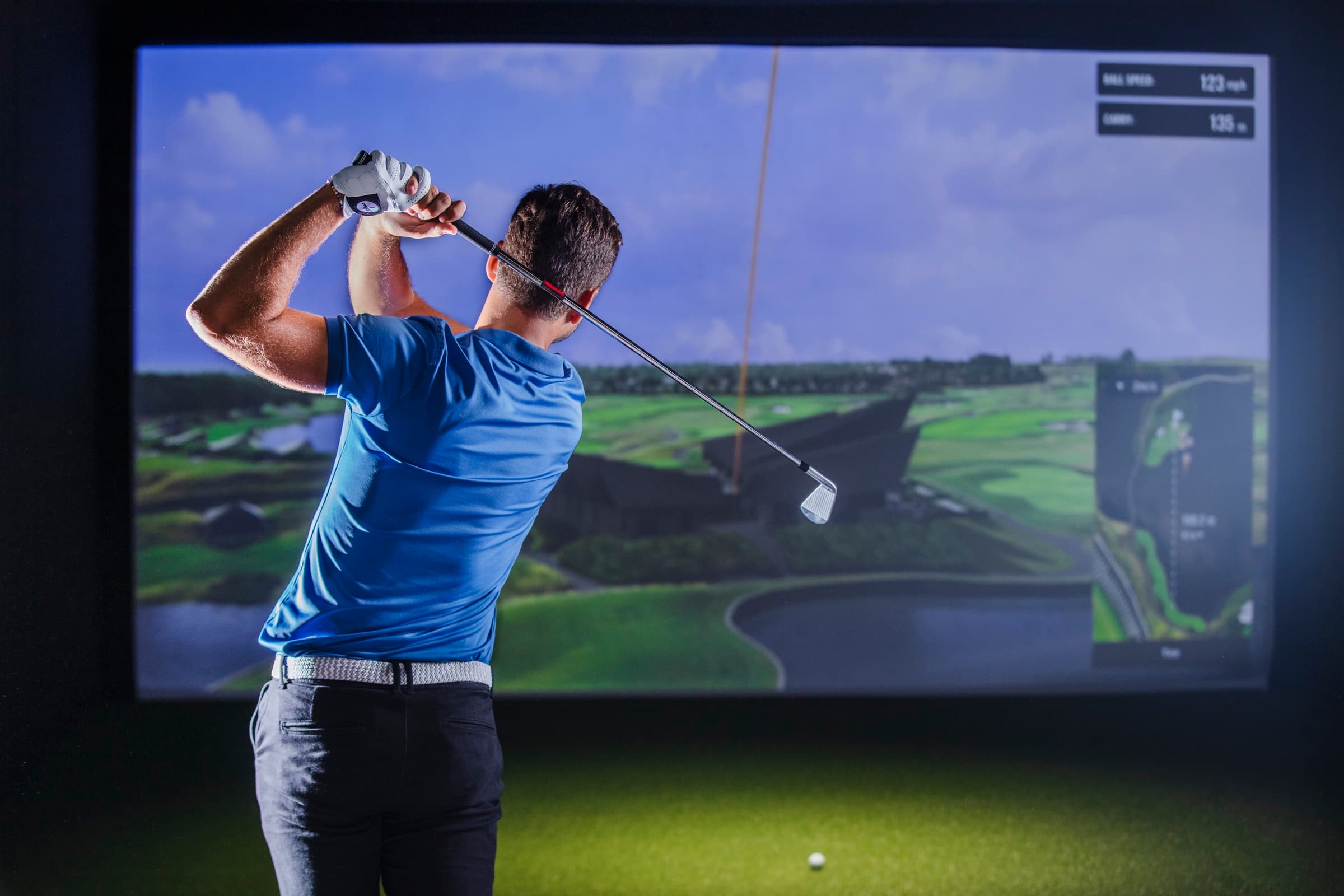 Golfspiller slår i en golfsimulator, skærmen viser boldhastighed og længde