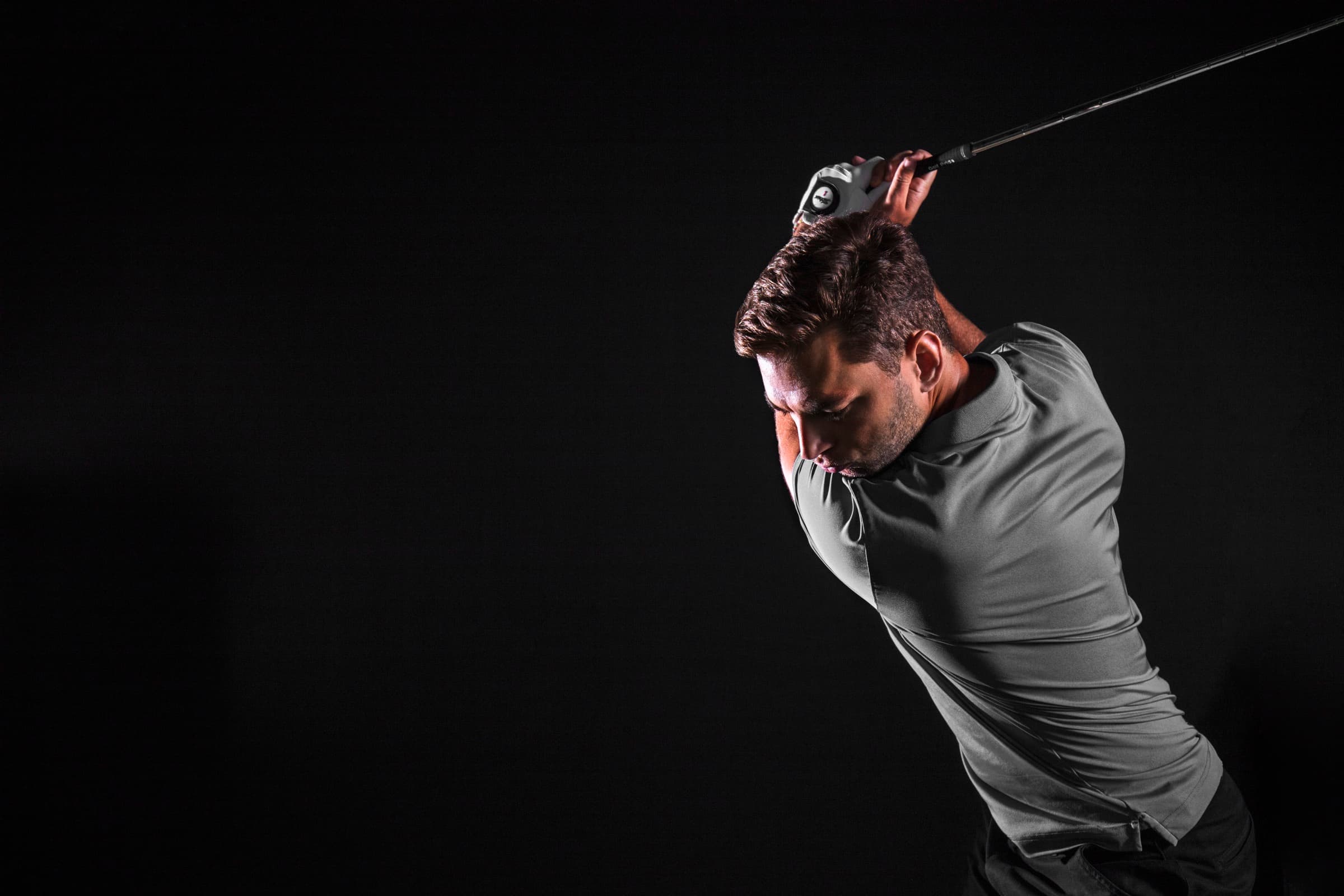 Golfspiller i gråt poloshirt fotograferet i studie mod sort baggrund, midt i baglænssvinget
